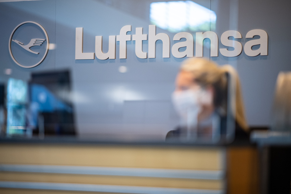 Eine Mitarbeiterin der Lufthansa sitzt mit ihrer Mund- und Nasenschutzmaske am Check-in im Flughafen Münster-Osnabrück. Die Lufthansa will ihr fliegendes Personal vollständig gegen Corona impfen lassen.