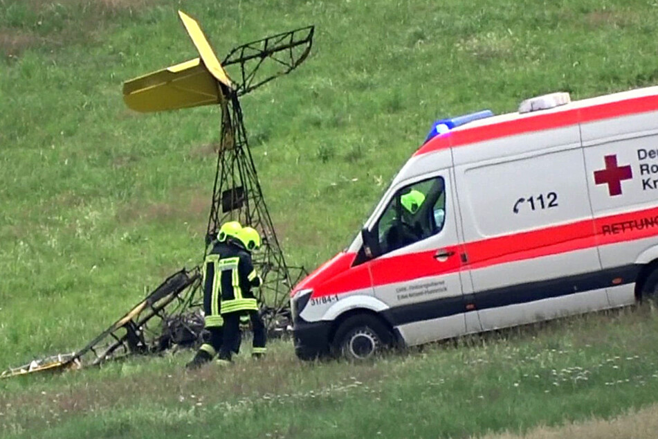 Rettungskräfte gehen nahe des Flugplatzes Mehren (Senheld) im Landkreis Vulkaneifel am Wrack eines einmotorigen Ultraleichtflugzeug vorbei.