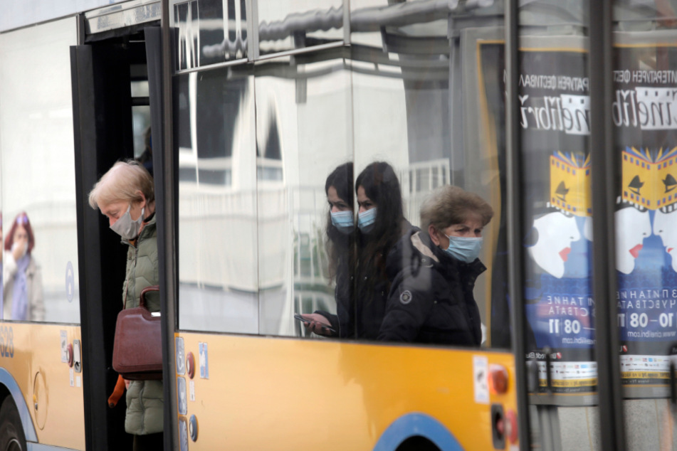 Fahrgäste tragen in Bulgarien Mund-Nasen-Bedeckungen und verlassen einen Bus, während andere darauf warten einzusteigen.