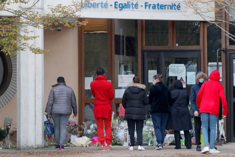 Schüler gedenken vor einer Schule, auf der der Schriftzug "Liberté - Egalité - Fraternité" (Freiheit - Gleichheit - Brüderlichkeit) zu lesen ist, einem Lehrer, der bei einer mutmaßlich terroristisch motivierten Tat ermordet wurde.