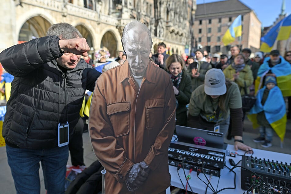 Ein Teilnehmer der Kundgebung auf dem Marienplatz gestikuliert neben einer Pappfigur des russischen Präsidenten Putin.