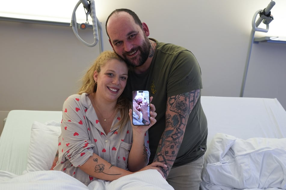 Linda und Mirko aus Haseldorf (Schleswig-Holstein) zeigen in einem Zimmer der Asklepios Klinik Altona auf ihrem Smartphone ein Foto von Tochter Evelynn.
