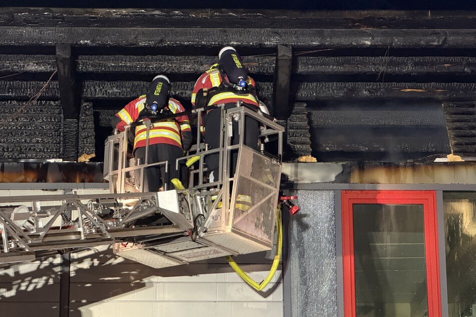 Feuerwehrleute inspizieren das völlig verkohlte Dach des Gebäudes.