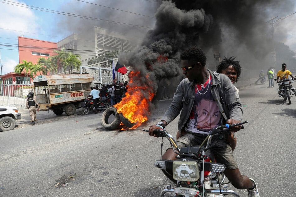 People drive past a burning blockade as demonstrators hold a protest in Port-au-Prince calling for the resignation of Haitian Prime Minister Ariel Henry.