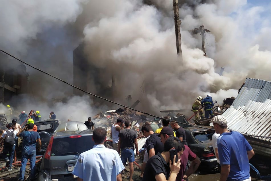 Zivilisten und Feuerwehrleute befinden sich an der Unfallstelle während Rauch aufsteigt.