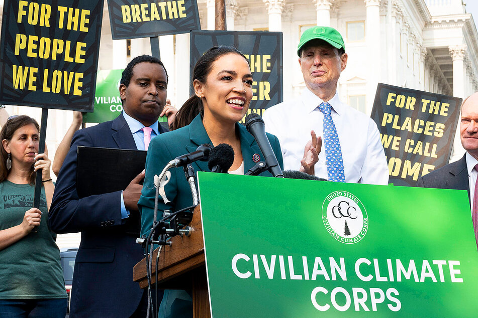 Rep. Alexandra Ocasio-Cortez speaks on the Climate Corps at a press conference in July 2021. Behind her are Rep. Joe Neguse (l.) and Sen. Ron Wyden.