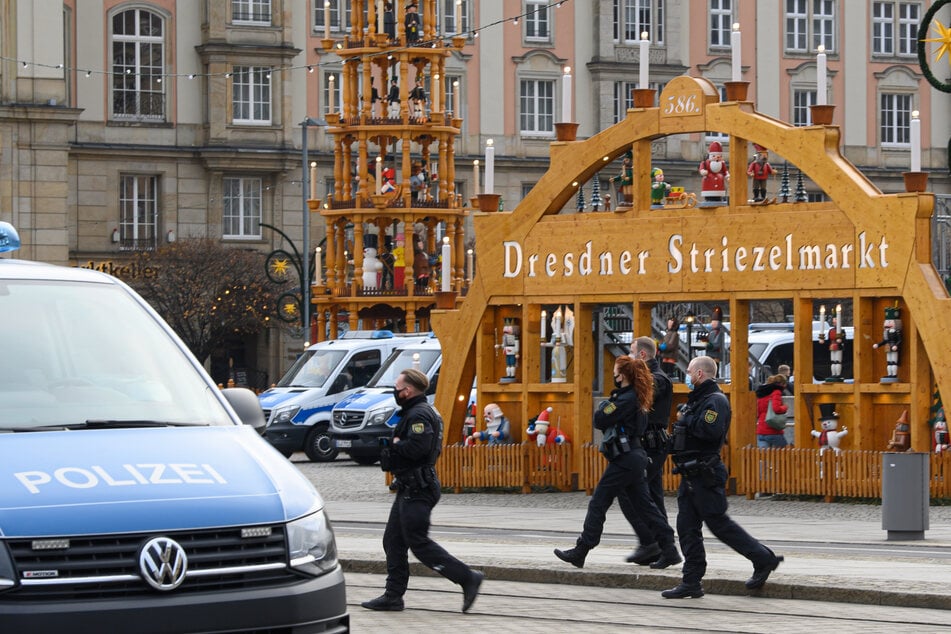 Die Beamten gehen vor einer Weihnachtspyramide und einem Schwibbogen des Striezelmarktes entlang.