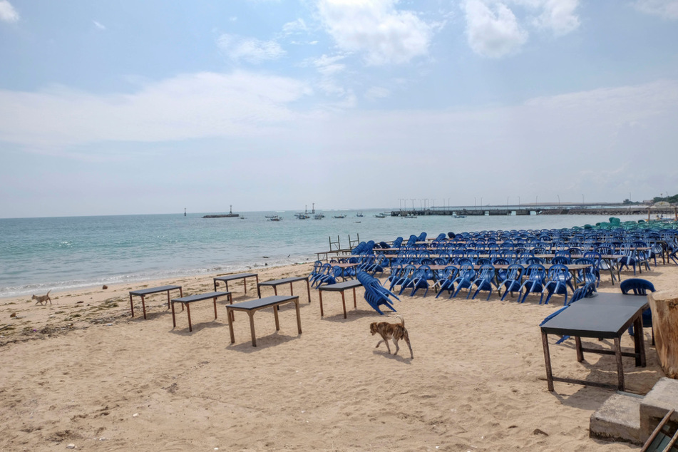 Ein Hund läuft am Jimbaran Beach zwischen Tischen eines leeren Fischrestaurants. Als "Insel der Götter" ist Bali bei Surfern, Badegästen und Yogis aus aller Welt bekannt.