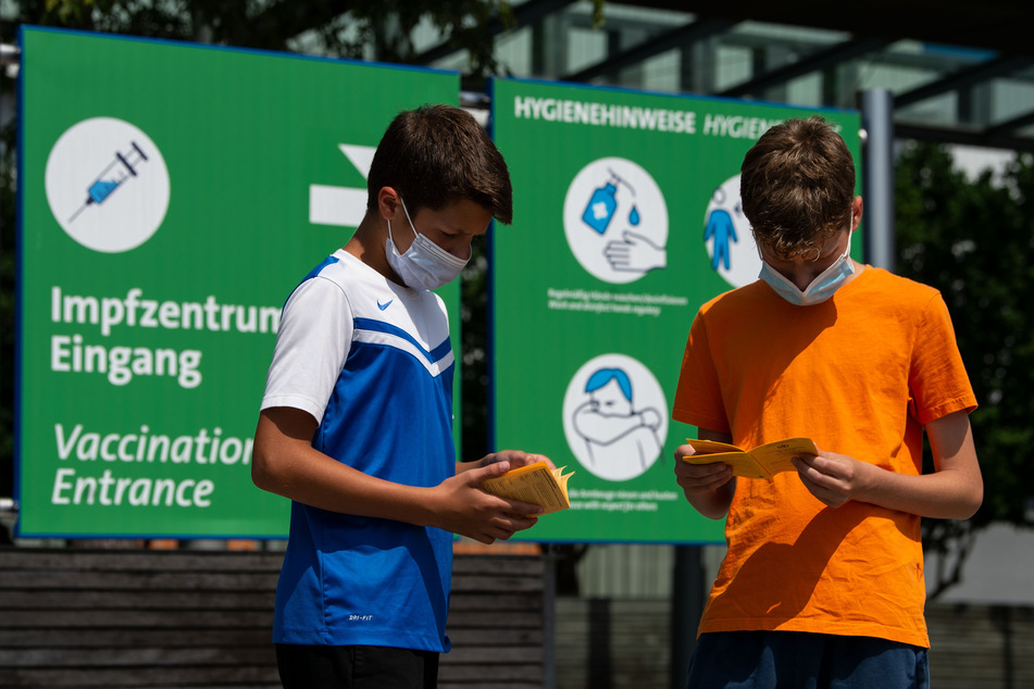 Zwei Kinder blättern vor einem Impfzentrum in ihrem Impfausweis. Auch in NRW können sich Zwölf- bis 15-Jährige jetzt grundsätzlich gegen das Coronavirus impfen lassen.
