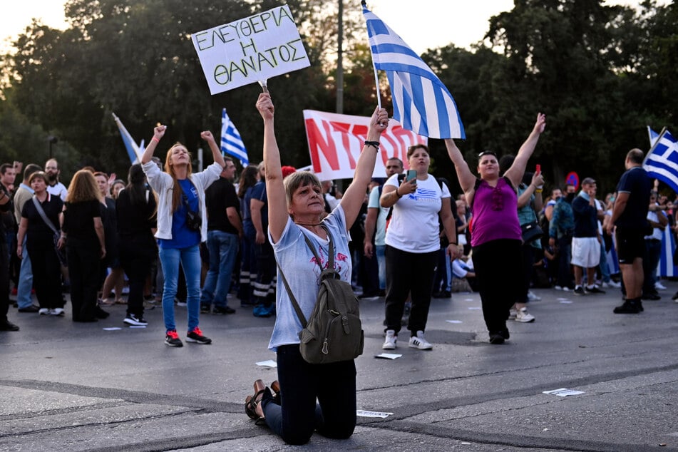 Eine Impfgegnerin kniet während einer Kundgebung. Hunderte Gegner von Corona-Schutzimpfungen haben vor dem Eingang des Messegeländes der Hafenstadt Thessaloniki Steine und andere Gegenstände auf die Polizei geschleudert.
