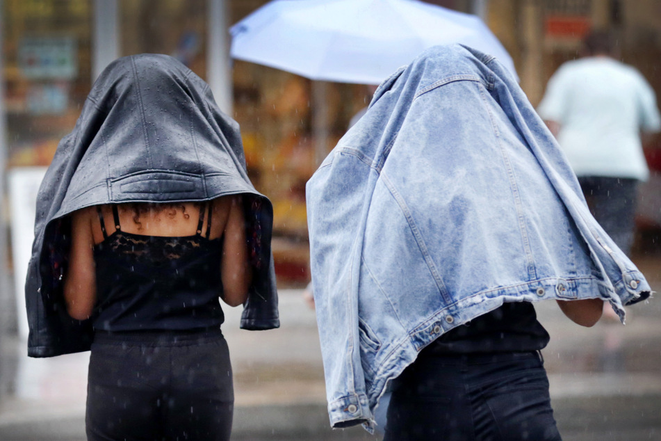 Zwei junge Frauen schützen sich mit ihren Jacken vor heftigem Regen. Das Wetter in NRW wird auch die nächsten Tage wieder ungemütlich.