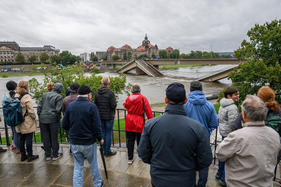 Schaulustige blicken auf den aktuellen Wasserstand und die eingestürzte Carolabrücke.