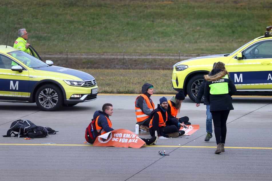 Vier Klimaaktivisten sitzen mit angeklebten Händen auf dem Zubringer einer Start-und Landebahn am Airport Franz-Josef-Strauß.