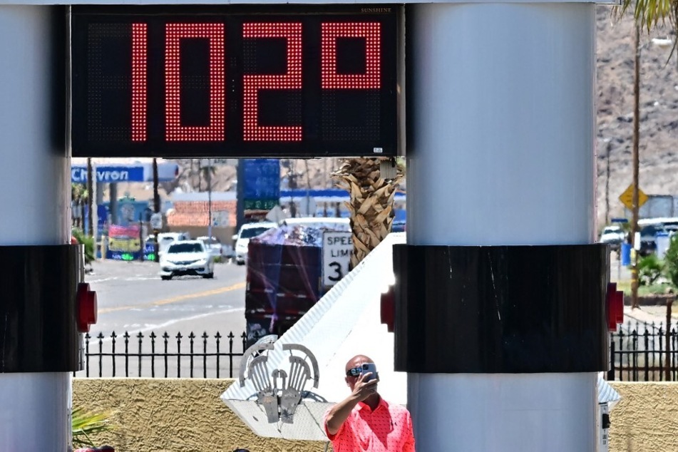 A man takes a selfie beside a thermometer showing 102°F in Baker, California, on July 11, 2023.