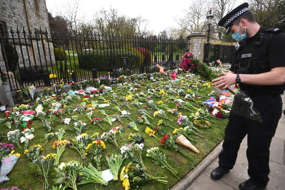 Ein Polizist hält einen Blumenstrauß und steht vor einer Grünfläche vor Schloss Windsor, auf der Blumen abgelegt wurden.
