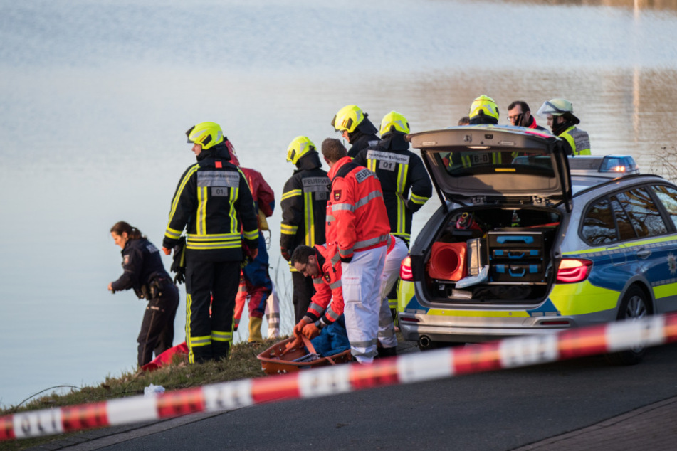 Einsatzkräfte der Polizei und Feuerwehr stehen am Ufer. (Symbolbild)