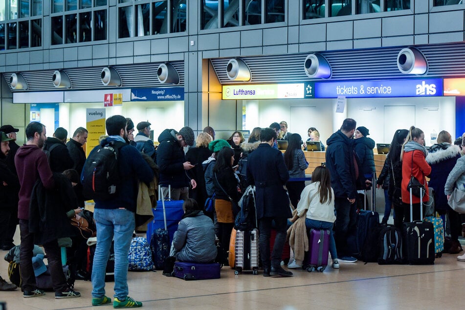 Fluggäste warten in der Abflughalle des Hamburger Flughafens vor einem Ticketschalter. Am Freitag könnten alle Flüge gestrichen werden. (Archivfoto)