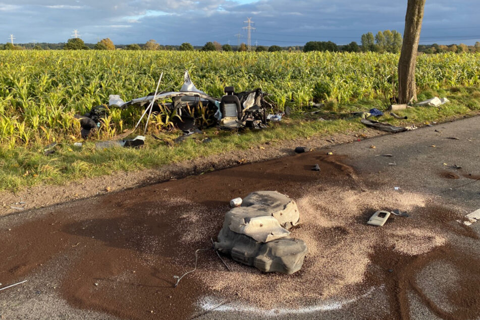 Trümmerteile liegen an der Unfallstelle auf der Straße. Auf einem Feld steht ein einzelner Autositz.
