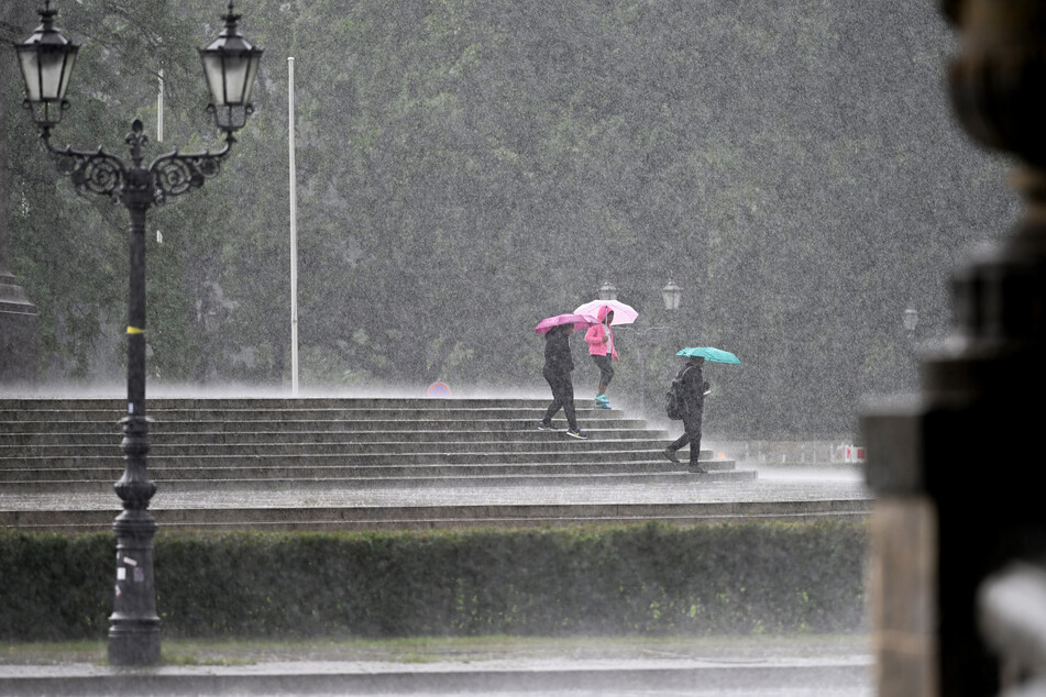 Touristen gehen bei starkem Regen die Stufen unterhalb der Siegessäule in Berlin hinunter.