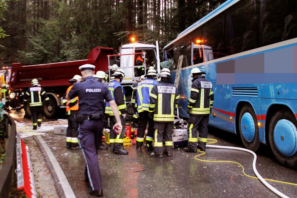 Einsatzkräfte von Polizei und Feuerwehr arbeiten an der Unfallstelle. Ein Lastwagenfahrer ist im Landkreis Rosenheim frontal in einen Schulbus gekracht.