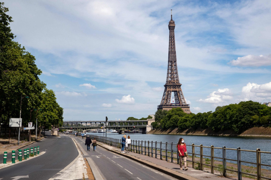 Menschen spazieren an der Seine neben dem Eiffelturm.