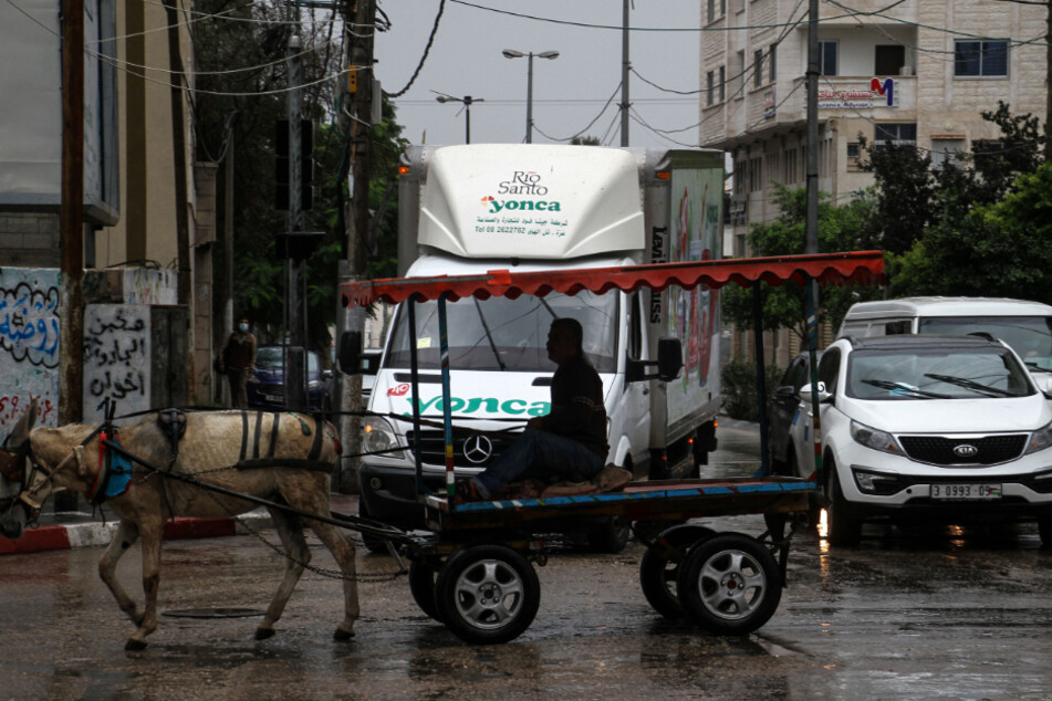 Gaza: Ein Palästinenser fährt bei Regen auf einem von einem Esel gezogenen Wagen im Straßenverkehr.