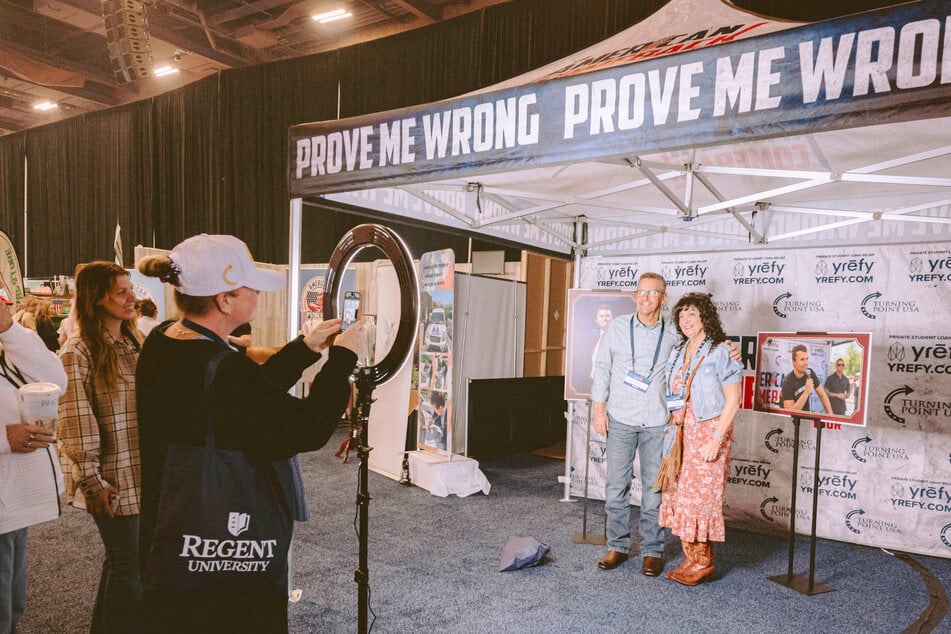 Charlie Kirk fans take souvenir photos with a replica of his assassination tent at TPUSA conference