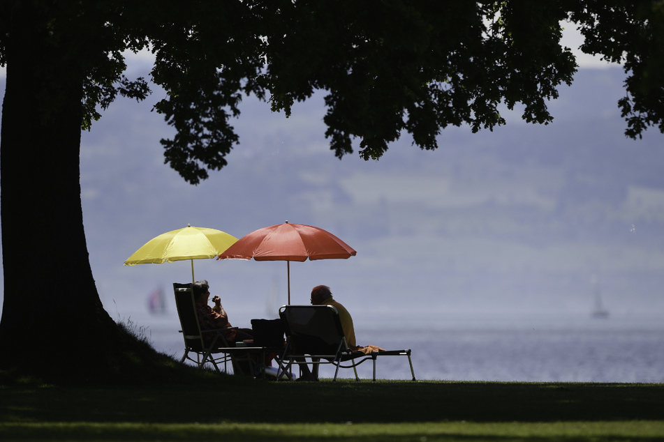 Zwei Badegäste sitzen an einem Strandbad am Ufer des Bodensees unter Sonnenschirmen. Am Strandbad in Wangen ereignete sich ein tödlicher Badeunfall. (Symbolbild)