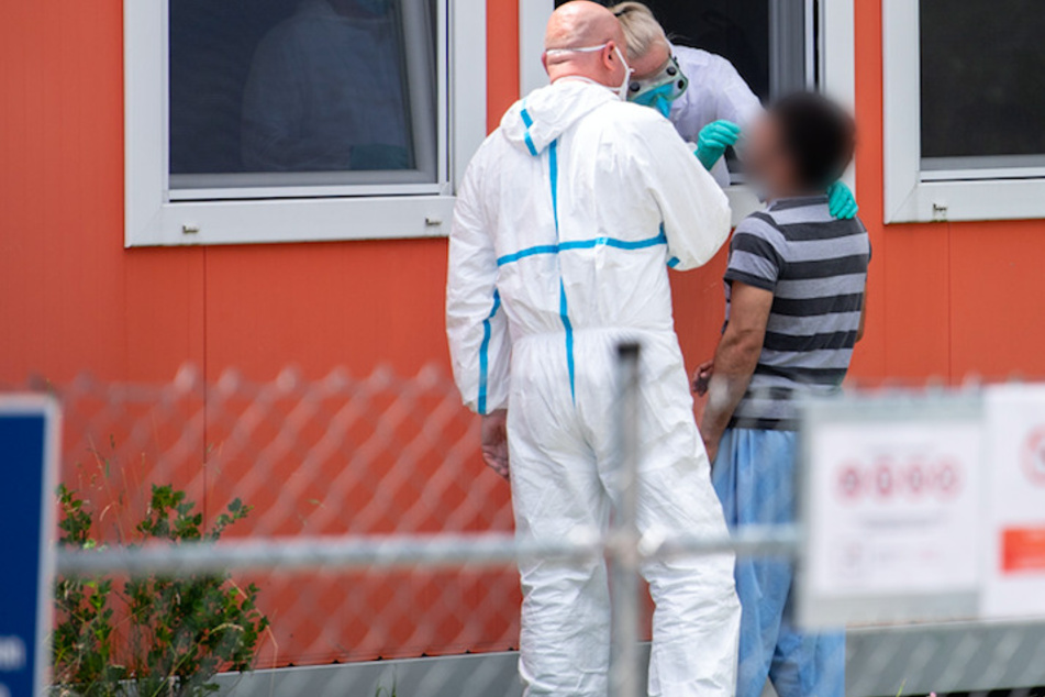 Eine Person im Schutzanzug nimmt einen Abstrich bei einem Bewohner der Anlage in Pöcking.