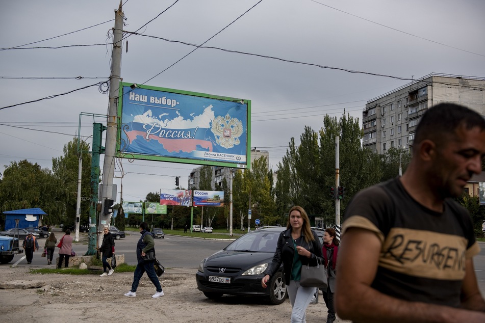 Menschen gehen in Luhansk an einem Plakat mit der Aufschrift "Unsere Wahl - Russland" vorbei.