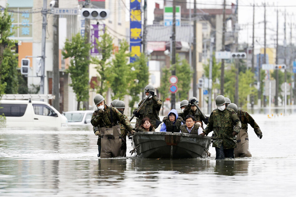 Mitglieder des japanischen Militärs retten Bewohner Omutas mithilfe eines Bootes auf einer überfluteten, von heftigen Regenfällen heimgesuchten Straße.