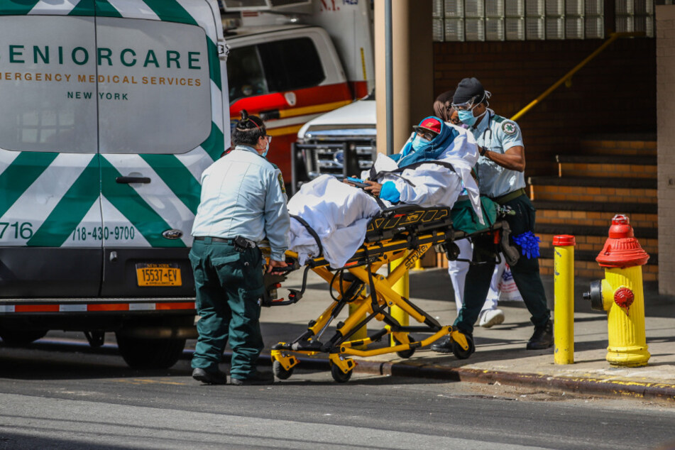 Sanitäter mit Mundschutz transportieren einen Patienten, der ebenfalls einen Mundschutz trägt, auf einer Trage vor dem Wyckoff Heights Medical Center in Brooklyn während der Corona-Pandemie.