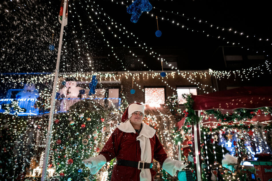 Dirk van Acken präsentiert als Weihnachtsmann verkleidet sein über und über mit Lichterketten geschmücktes Weihnachtshaus.