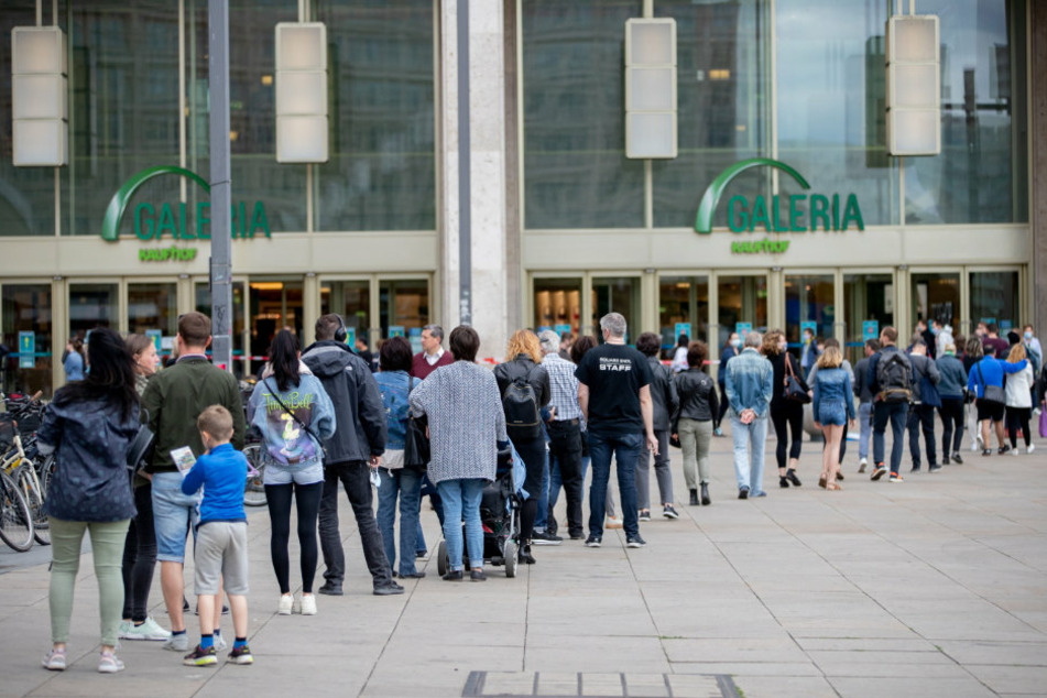 Menschen stehen auf dem Alexanderplatz in einer langen Schlange um bei Galeria Kaufhof einzukaufen.