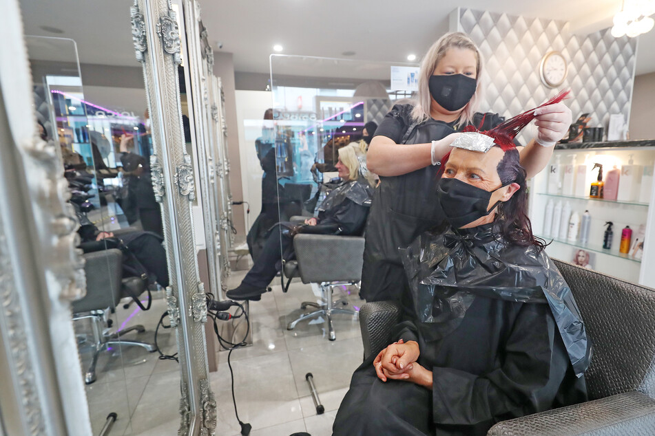 Eine Frau lässt sich mit Mundschutz bei einem Friseur die Haare färben. (Archivbild)