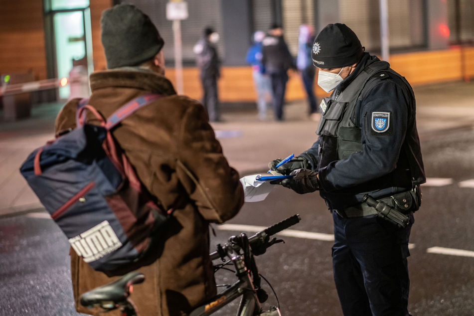 Ein Polizist nimmt die Personalien eines Radfahrers auf, der trotz einer nächtlichen Ausgangsbeschränkung unterwegs ist. (Symbolfoto)