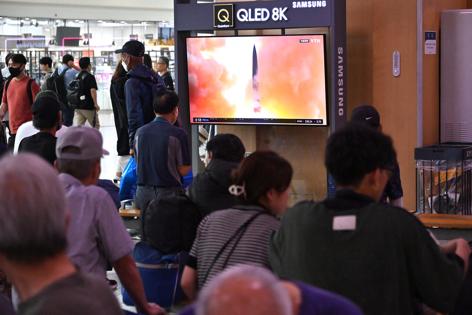 People watch a television screen showing a news broadcast with file footage of a North Korean missile test, at a railway station in Seoul on September 13, 2023.