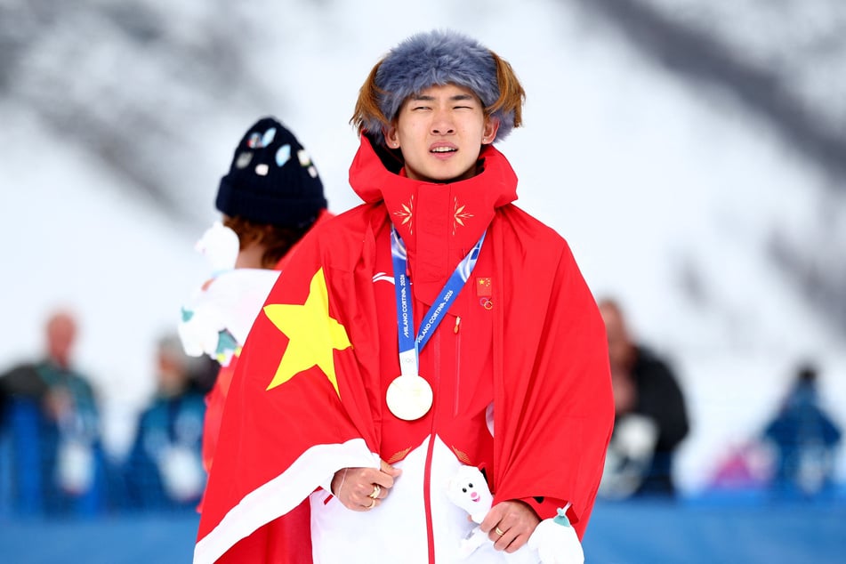 Gold medalist Yiming Su of China celebrates on the podium after winning the Men's Snowboard Slopestyle Final at the Milan Cortina Olympics on February 18, 2026.