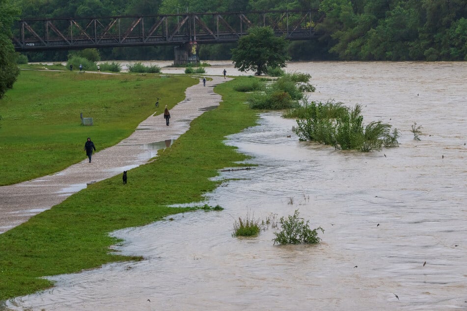 Passanten gehen am Ufer der Hochwasser führenden Isar entlang. Das Wasserwirtschaftsamt München gab eine Hochwasserwarnung heraus. (Archiv)