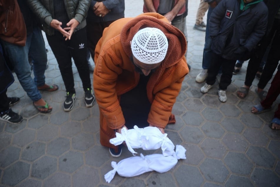 A Palestinian man puts the shrouded body of newborn Jumaa al-Batran, who reportedly died due to hypothermia, next to the shrouded corpse of another child ahead of their funeral at the Aqsa Martyrs hospital in Deir el-Balah on December 29, 2024.