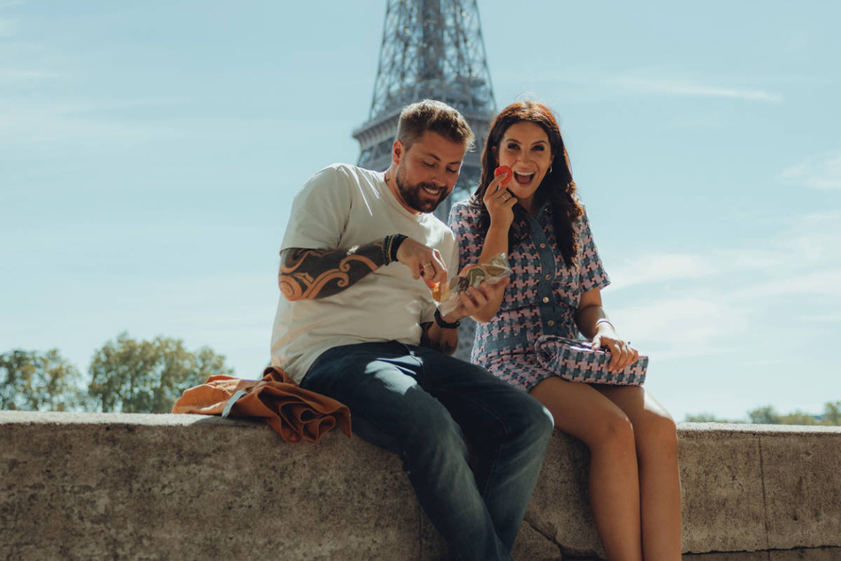 Felix von Jascheroff (41) und Chryssanthi Kavazi (34) genießen eine Drehpause vor dem Hintergrund des Eiffelturms.