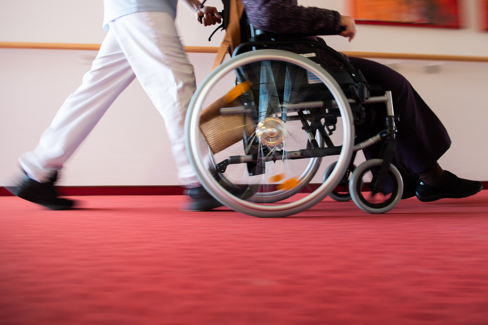 Ein Pfleger schiebt eine Seniorin mit einem Rollstuhl.