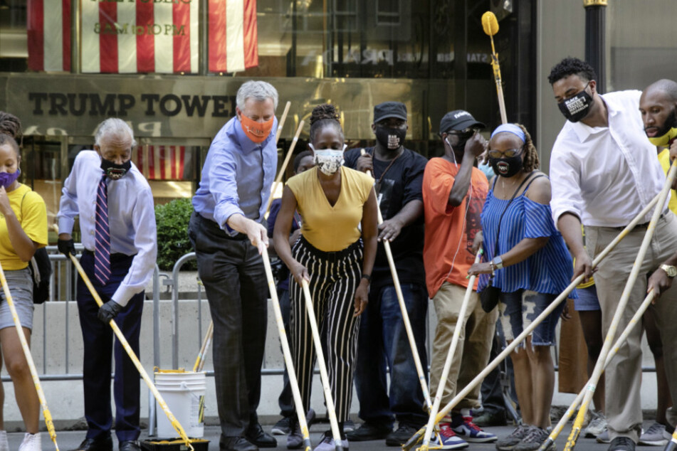 USA, New York: Bill de Blasio (3.v.l), Bürgermeister von New York, hilft gemeinsam mit seiner Ehefrau Chirlane McCray (4.v.l) und dem US-Amerikanischen Bürgerrechtler Al Sharpton (2.v.l) im Rahmen einer Protestaktion dabei, den Schriftzug "Black Lives Matter" auf die Fifth Avenue vor dem Trump Tower zu malen.