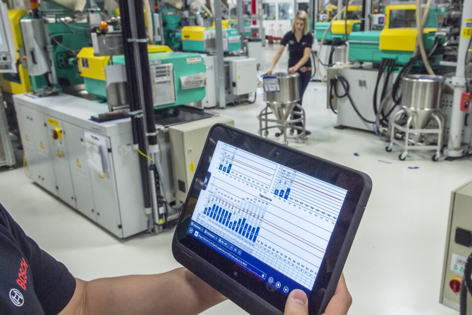 Ein Bosch-Mitarbeiter überprüft mit einem Tablet die Betriebsdaten von vernetzten Maschinen für Metallspritzguss.