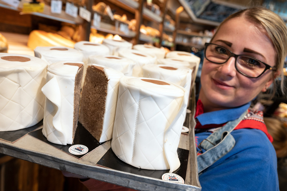 Eine Verkäuferin der Bäckerei Schürener Backparadies zeigt im Verkaufsraum ein Blech mit runden Marmorkuchen, die mit Fondant umwickelt wie Toilettenpapier-Rollen aussehen.