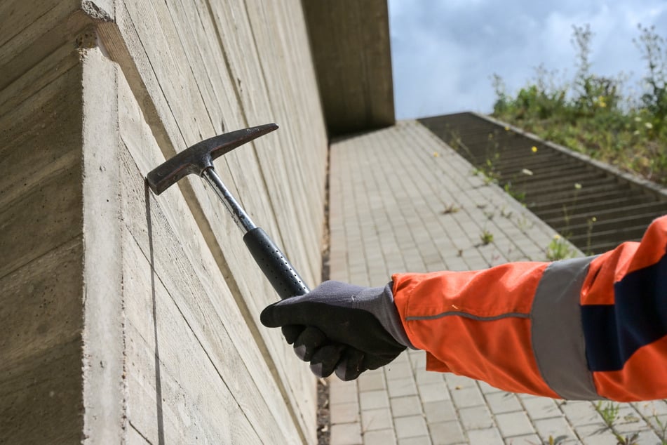 Mit einem Hammer wird eine Autobahnbrücke der A71 auf Bauwerksschäden kontrolliert.