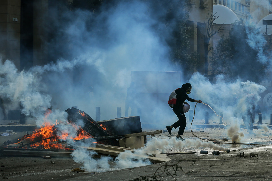 Ein Demonstrant in Beirut versucht während Zusammenstößen mit Bereitschaftspolizisten einen Tränengaskanister zu löschen.