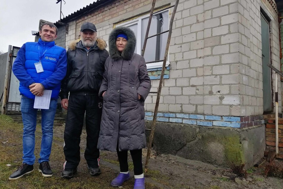 Ein Helfer neben Valentina (64) und Oleksandr Tkachenko (68, M.), die wieder in ihr Haus zurückkehren konnten, nachdem Dach, Fenster und Heizung repariert wurden.