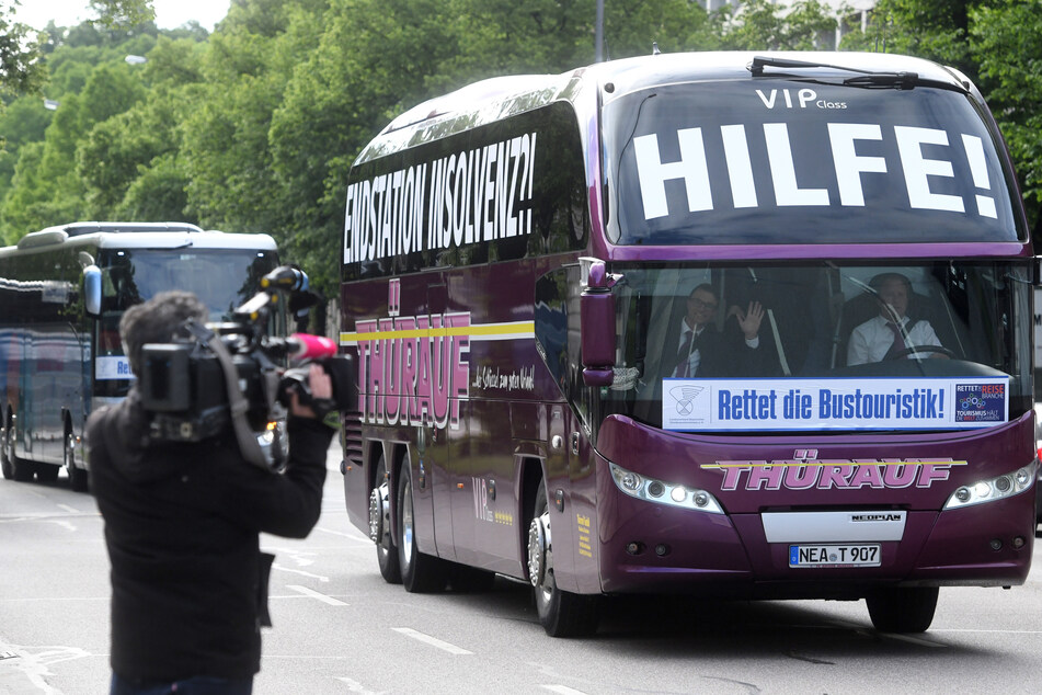 Ein Kameramann filmt den Demonstrationszug von Reisebussen, wobei ein Reisebus mit den Schriftzügen "Hilfe!" und "Rettet die Bustouristik" beklebt ist.