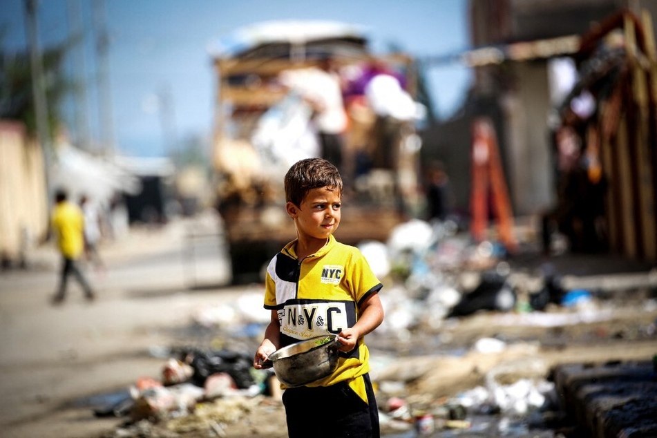 A Palestinian boy holds a pot of food as people leave a camp in Rafah, bound for central Gaza, as Israel bombs and prepares to invade the city.